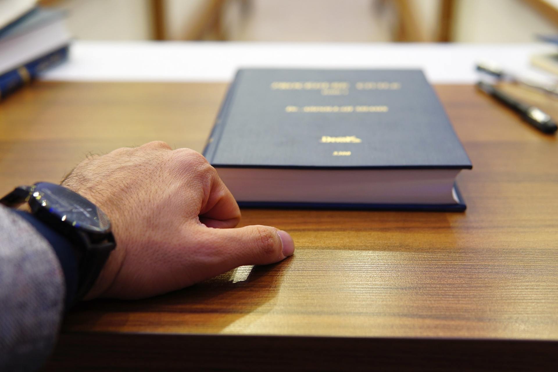 Una mano posata su un codice rilegato in blu, sulla scrivania